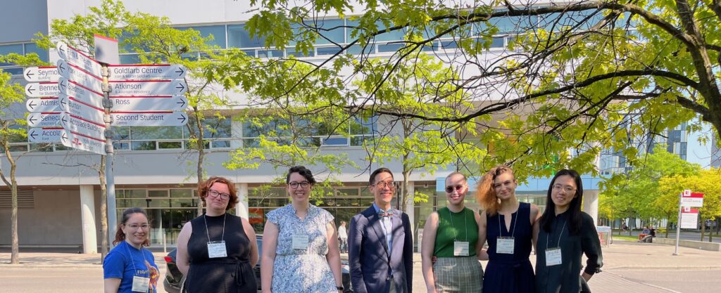 A lineup of seven lab members standing outside a building on the campus of York University.
